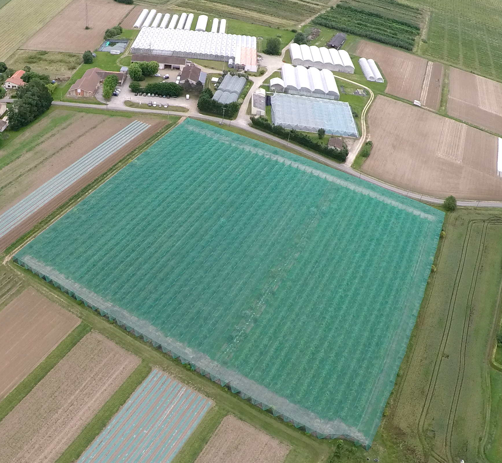 Photo du site avec en premier plan un verger de pommier en AB, puis les bâtiments d'exploitation et les bureaux puis les serres et les parcelles de culture